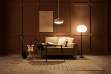 Interior of stylish living room with cozy sofa, coffee table and glowing lamps at evening