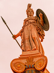 Statue of Athena, the Greek goddess of wisdom and knowledge, with helmet, a sharp spear and shield on a gold gilded column. craftsmanship highlights the power of the deity, set in a timeless backdrop.