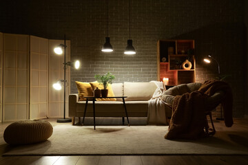 Interior of stylish living room with cozy grey sofa, armchair, coffee table and glowing lamps at...