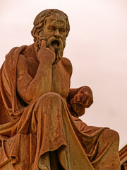 Seated marble statue of Socrates, the ancient Greek philosopher, set against a dramatic backdrop in Athens, Greece. Representation of wisdom and intellectual inquiry.