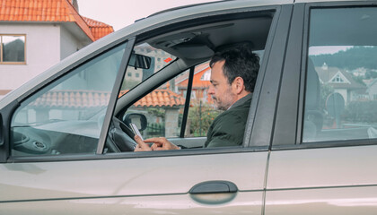 middle-aged man checking his cell phone in the car