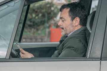 middle-aged man checking his cell phone in the car
