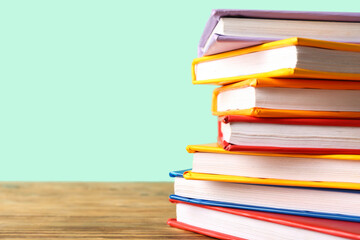 Stack of colorful books on wooden table against turquoise background