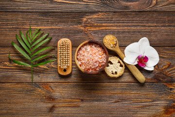 Beautiful spa composition with bowl of sea salt and bath supplies on brown wooden background