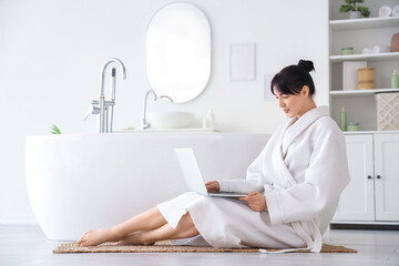 Young woman in waffle robe using laptop on rug at home