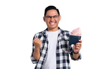 Excited young Asian man in casual shirt holding wallet full of cash, celebrating financial success...