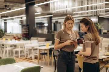 Two Women Discussing While Browsing a Mobile Phone in Modern Furniture Store