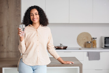 Young African-American woman with glass of water in kitchen