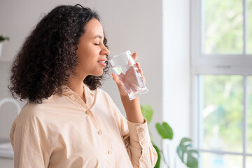 Young African-American woman drinking water in kitchen
