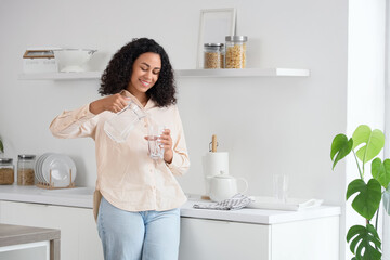 Young African-American woman pouring water into glass in kitchen