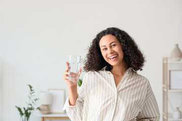 Happy young African-American woman with glass of water at home
