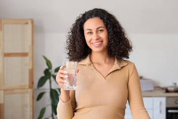 Young African-American woman with glass of water in kitchen