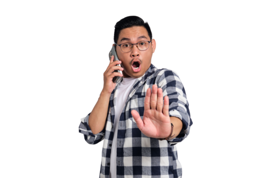 Surprised young Asian man in casual shirt talking on smartphone and making stop sign with hand isolated on transparent background