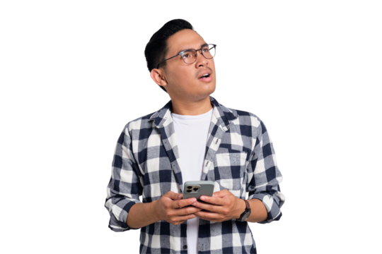 Doubtful young Asian man in casual shirt holding smartphone, looking aside at free space, thinking about something isolated on transparent background