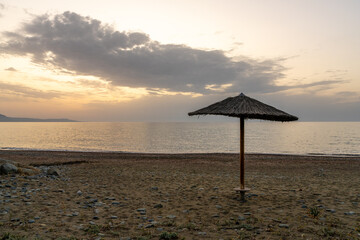 Lone straw umbrella on quiet seaside at golden hour. Idyllic summer scene, ideal for travel ads,...