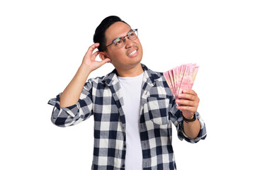 Financial planning. Pensive young Asian man in casual shirt holding money and looking up, thinking...