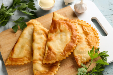 Board with tasty chebureks and fresh vegetables on grey grunge table