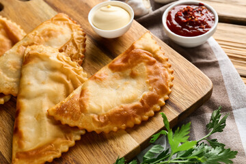 Board with tasty chebureks, fresh parsley and sauces on wooden table