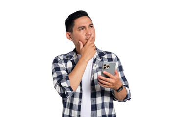 Pensive young Asian man in casual shirt holding smartphone, looking aside at copy space, thinking...