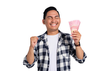 Excited young Asian man in casual shirt holding money and clenching fist, celebrating financial success isolated on transparent background. Profit and wealth concept