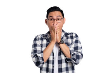 Surprised young Asian man in casual shirt covering mouth with hand, looking at camera with amazed facial expression isolated on transparent background