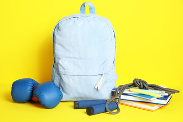 Backpack, school supplies and sports equipment on yellow background