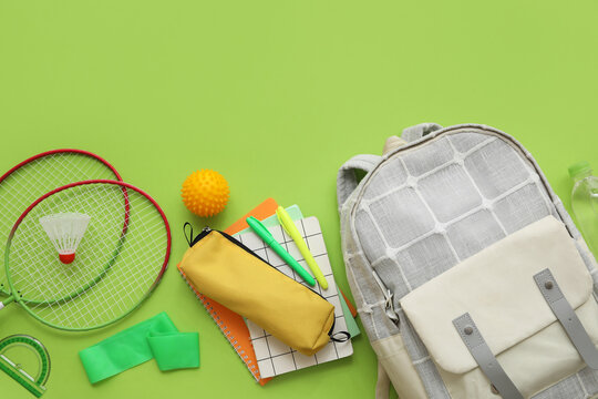 Composition with backpack, school supplies and sports equipment on green background
