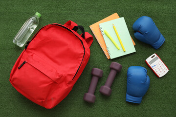 Composition with backpack, school supplies and sports equipment on green grass background