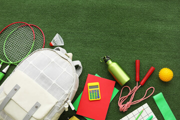 Composition with backpack, school supplies and sports equipment on green grass background
