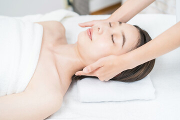 エステサロンで頭部をマッサージされる若い女性