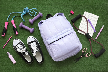 Composition with backpack, school supplies and sports equipment on green grass background
