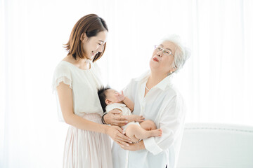 赤ちゃんを抱っこするシニア女性と見守る女性