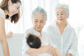 赤ちゃんを抱っこするシニア女性と見守る女性たち
