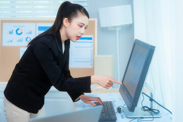 Attractive Asian woman in a formal black suit works attentively at her desk, writing notes. She embodies professionalism and focus while managing tasks in a well-organized office environment.
