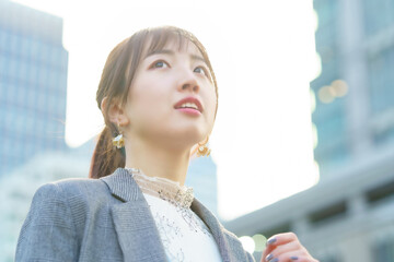 ビル街で空を見上げる若い女性