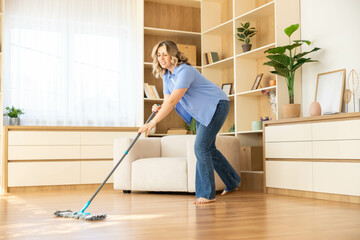 A woman appears focused and slightly strained while mopping the floor, showing the effort that...