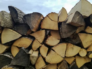 Gordijnen Woodpile. Chopped firewood is stacked in neat piles on blue sky background. Natural energy raw material. Background. Close-up. Selective focus. © Marina_Nov