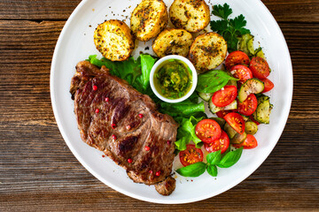 Grilled beef steak with baked potatoes and fresh salad on wooden table	