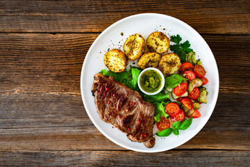 Grilled beef steak with baked potatoes and fresh salad on wooden table	