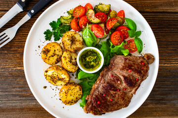 Grilled beef steak with baked potatoes and fresh salad on wooden table	