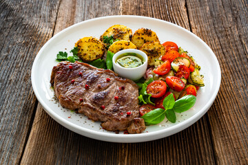 Grilled beef steak with baked potatoes and fresh salad on wooden table	