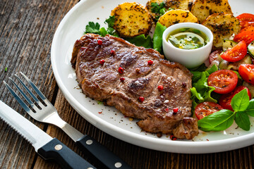 Grilled beef steak with baked potatoes and fresh salad on wooden table	