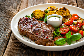Grilled beef steak with baked potatoes and fresh salad on wooden table	