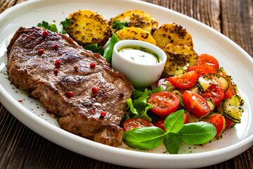 Grilled beef steak with baked potatoes and fresh salad on wooden table	