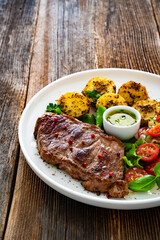 Grilled beef steak with baked potatoes and fresh salad on wooden table	