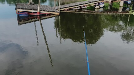 River landscape during fishing. POV, first person view on float rod lies on river bank, the float in the water sways on waves. Active recreation on fishing on lake, on river, on reservoir.