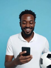 Man smiles holding smartphone  soccer ball against a blue background