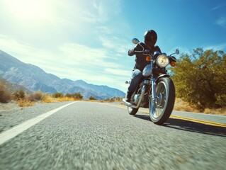 Motorcycle rider in helmet heads down a desert road with mountains and blue sky