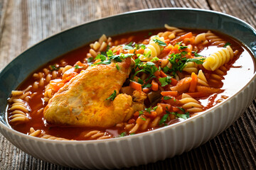 Tomato soup with chicken thigh and noodles on wooden table