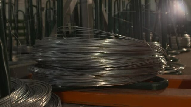 A close-up view of a large, tightly wound coil of galvanized steel wire resting on an orange industrial surface.